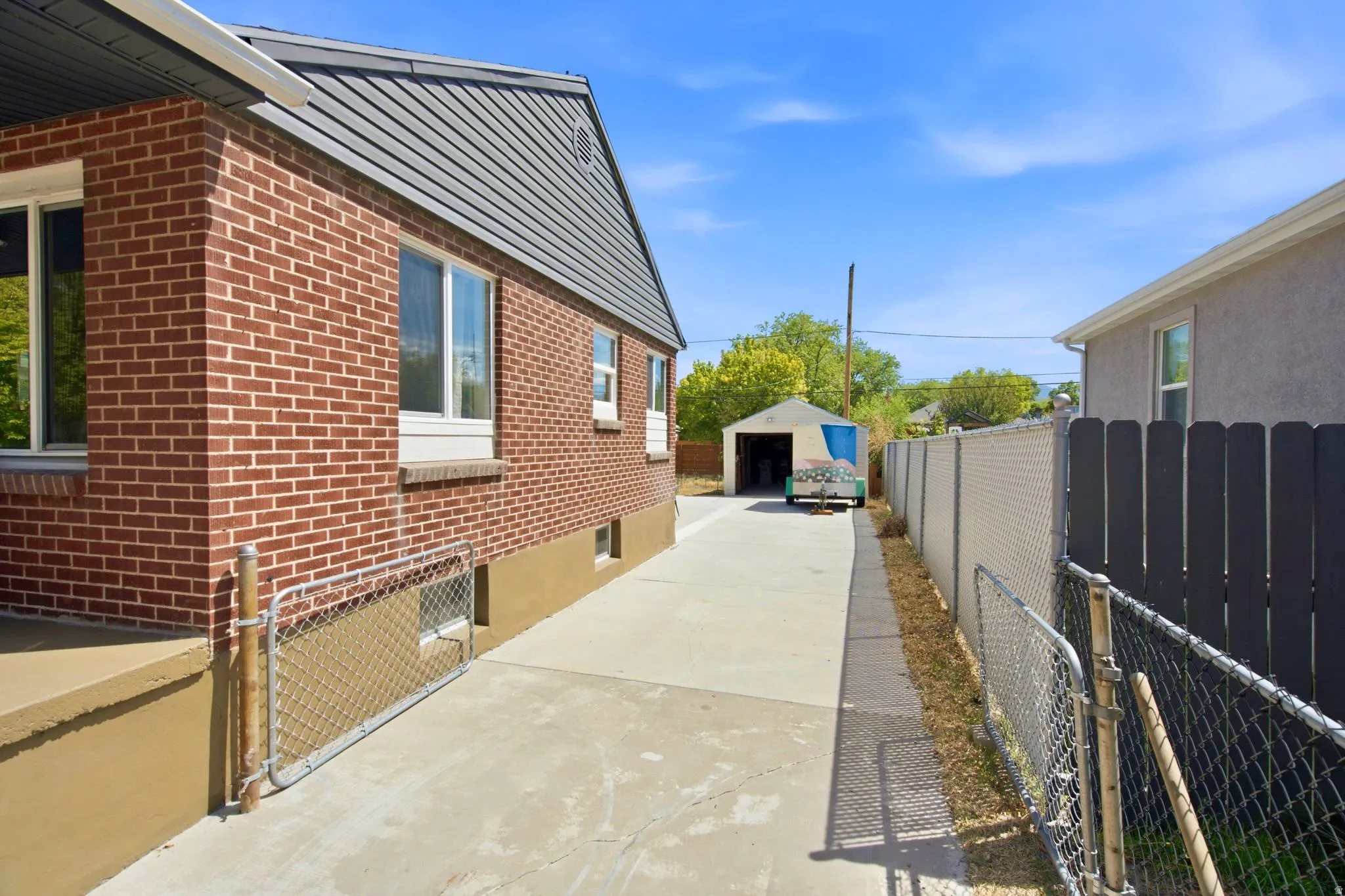 Brick exterior with multiple windows, concrete driveway, and chain-link fencing