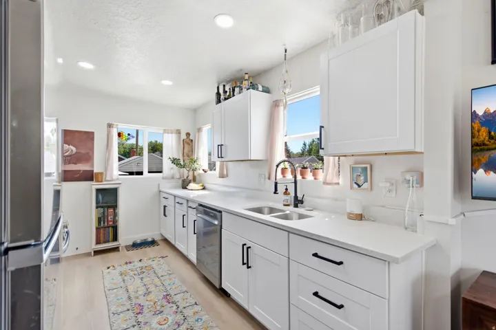 White shaker-style cabinetry with matte black hardware, stainless steel dishwasher, white countertops, and dual-basin sink with a gooseneck faucet