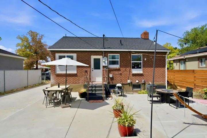 Brick exterior with a dark shingle roof, concrete patio, and a wood privacy fence