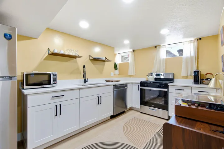 White shaker cabinetry, stainless steel appliances, white countertops, built-in shelving, and recessed lighting