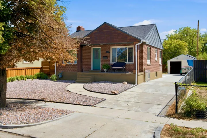 Brick exterior with a gabled roof and siding, featuring a covered porch, established trees, and a detached garage with a long driveway