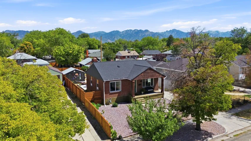 Brick exterior with a covered front porch, dark shingle roof, wood-paneled siding accent, and a fenced yard