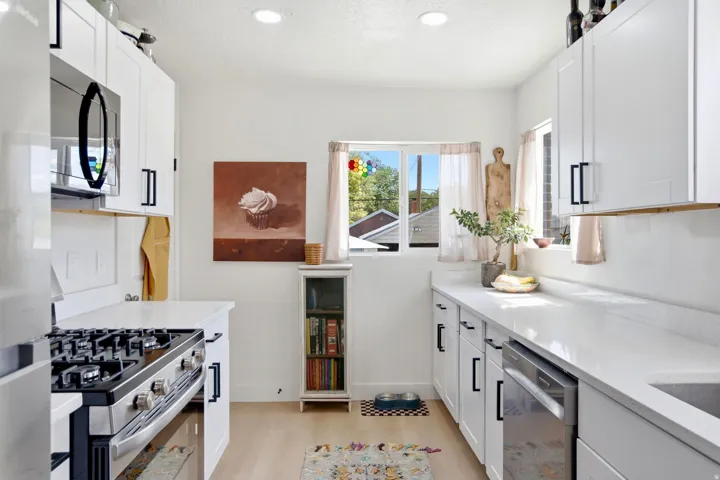 White cabinetry with black hardware, stainless steel appliances, light wood-finish flooring, recessed lighting, and a built-in oven range