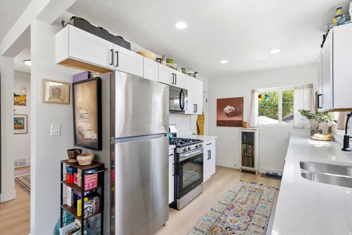 White cabinetry with black hardware, stainless steel appliances, light-toned wood-finish flooring, recessed lighting, and a double basin sink