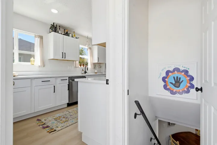 Kitchen featuring white cabinetry, light-toned countertops, a stainless steel dishwasher, and wood-finish flooring