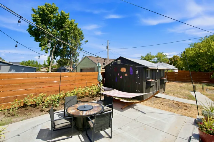 Concrete patio with string lighting, wood privacy fence, and a detached structure