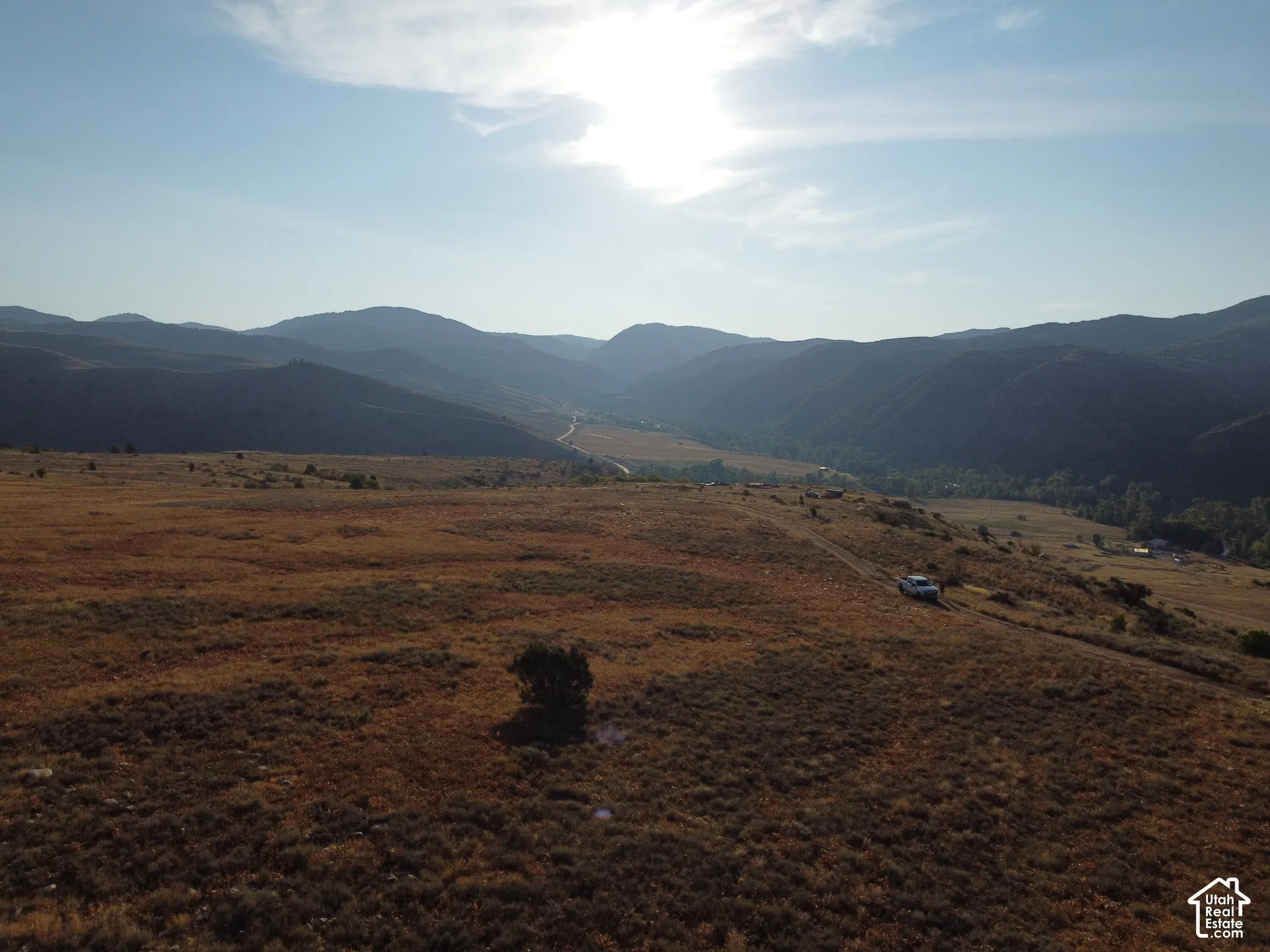 Expansive open terrain featuring natural vegetation, a distant valley, and surrounding mountains