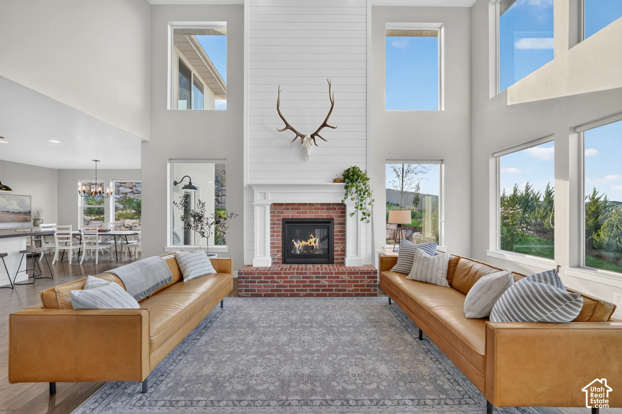 Spacious living area featuring a brick fireplace with a white mantel, high ceilings, and abundant natural light from multiple windows