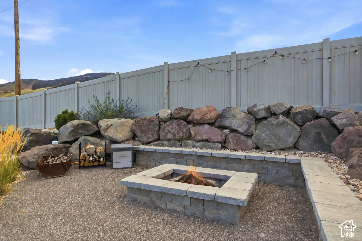 Gravel patio with a built-in stone fire pit, stone retaining wall, and privacy fencing
