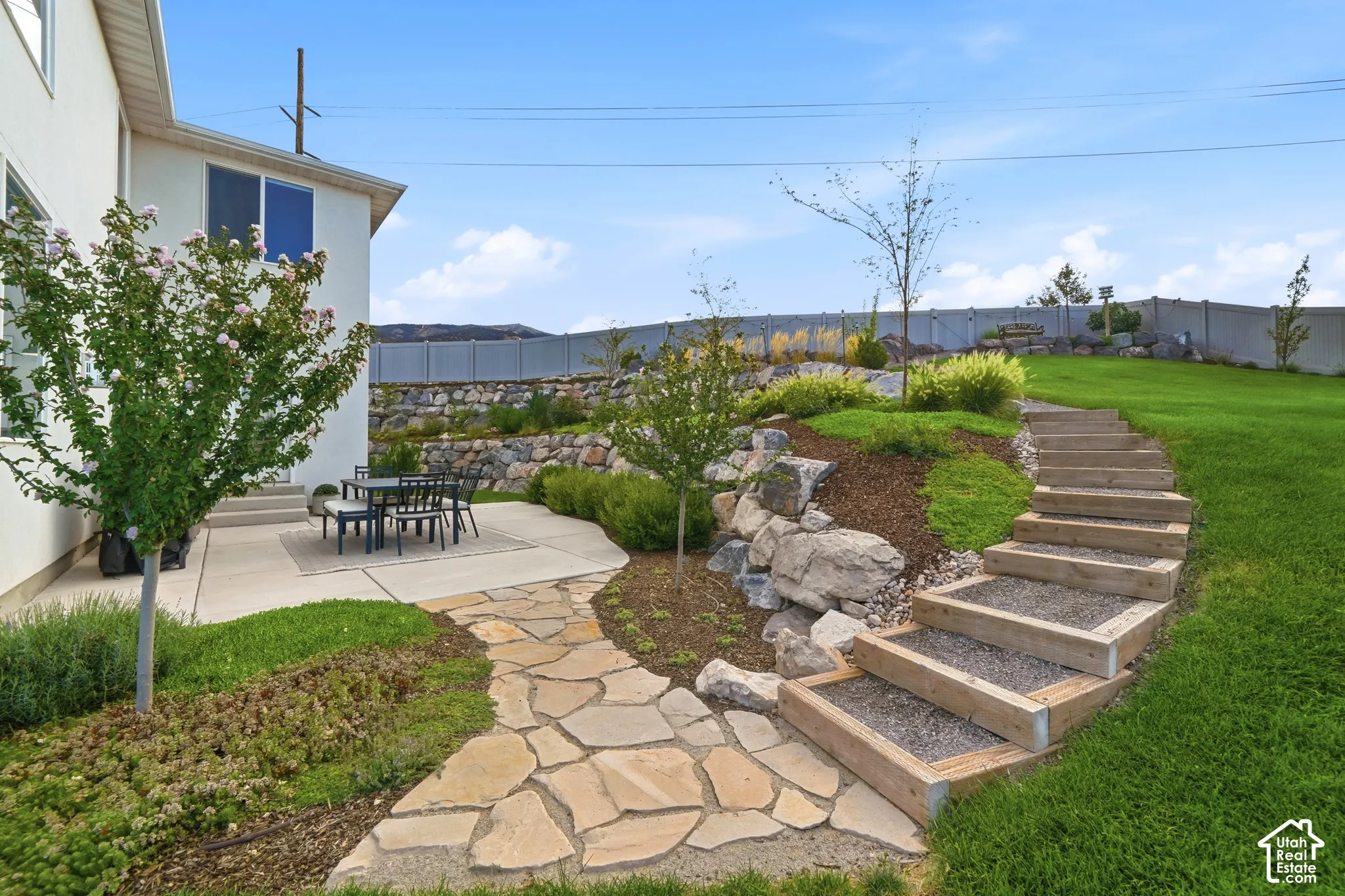 Concrete patio, flagstone pathway, terraced landscaping with rock retaining walls, and wood-framed garden steps