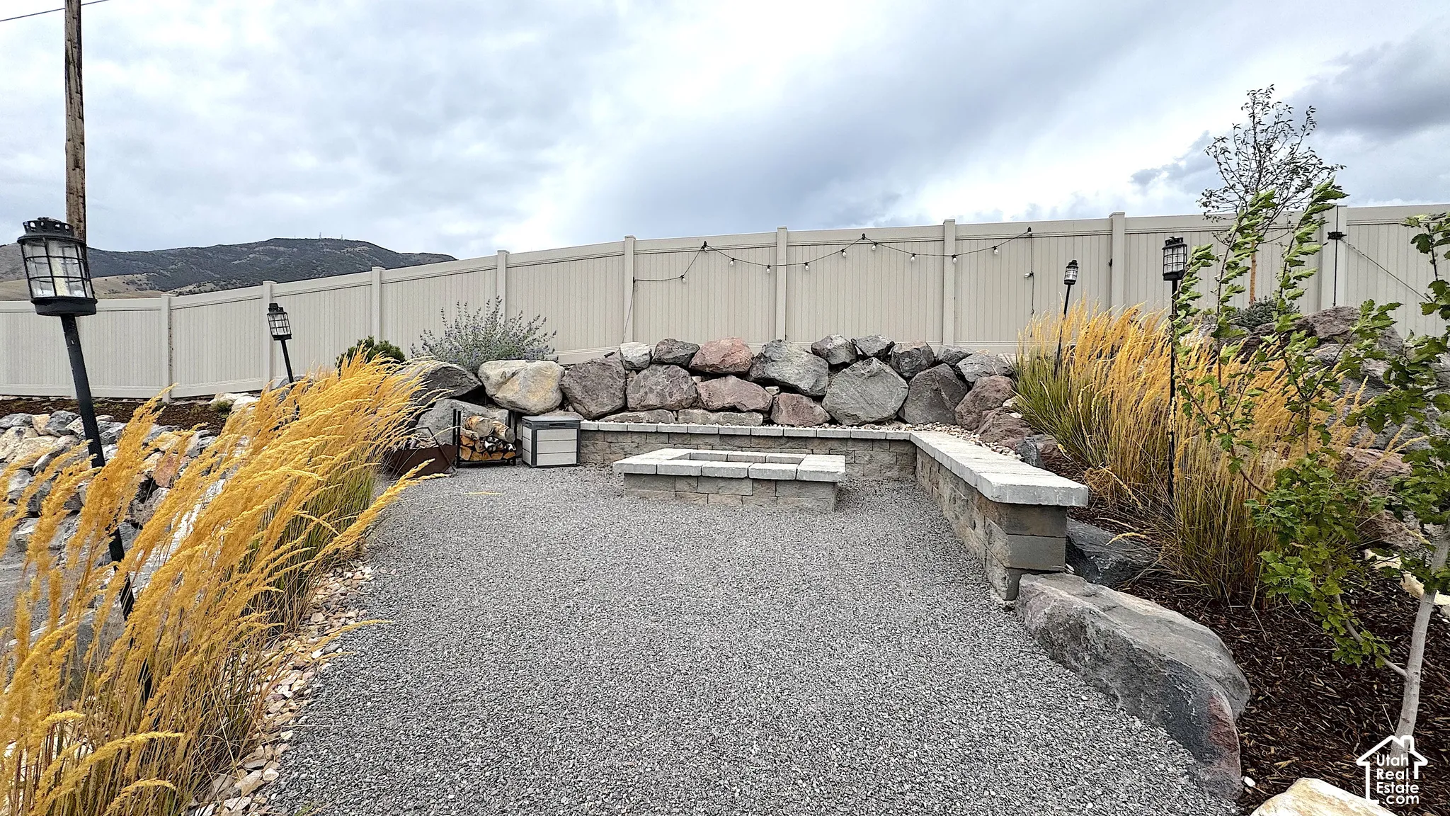 Gravel patio area featuring a built-in fire pit, stone retaining walls, and mature landscaping