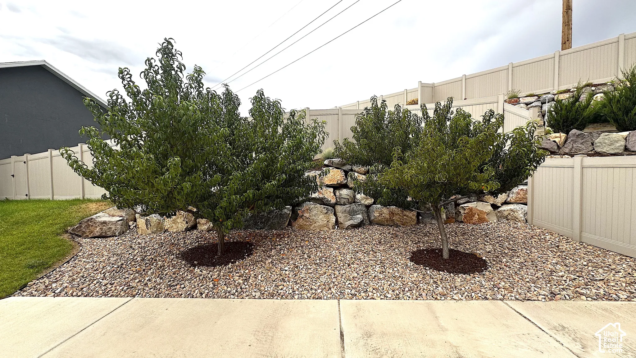 Decorative gravel landscaping with mature plantings, a concrete pathway, a rock retaining wall, and a privacy fence