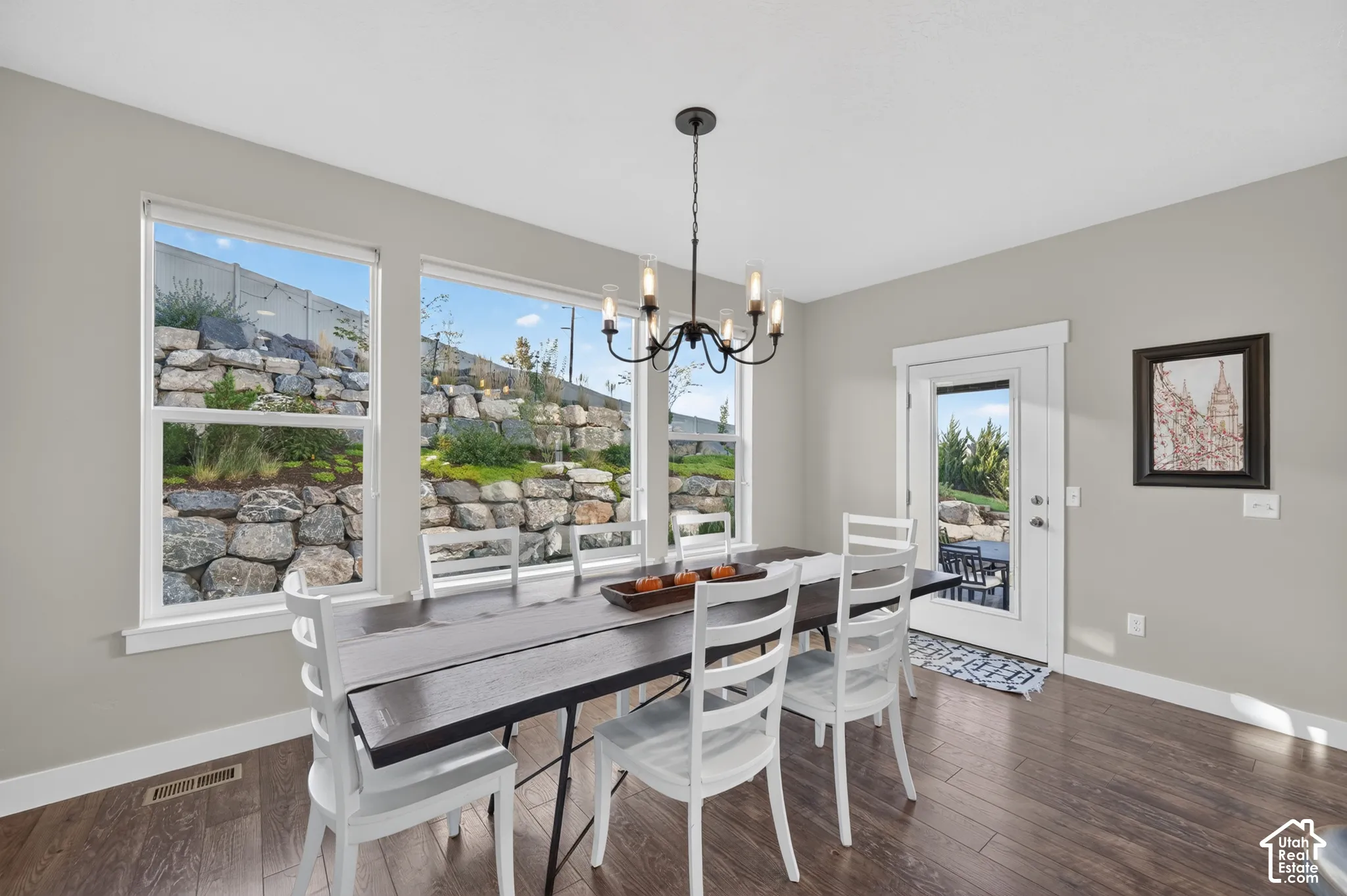 Wood-finish flooring, multiple large windows, glass-paneled exterior door, and an overhead chandelier