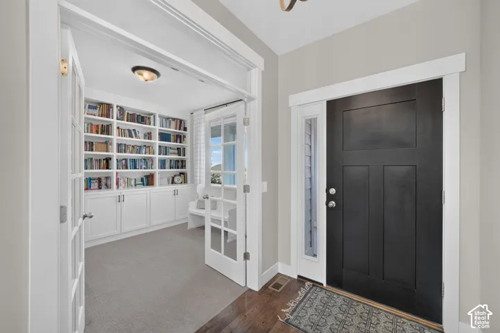 Entryway featuring a dark wood-finish door with sidelight, wood-finish flooring, and a cased opening to a room with built-in shelving, cabinetry, and French doors