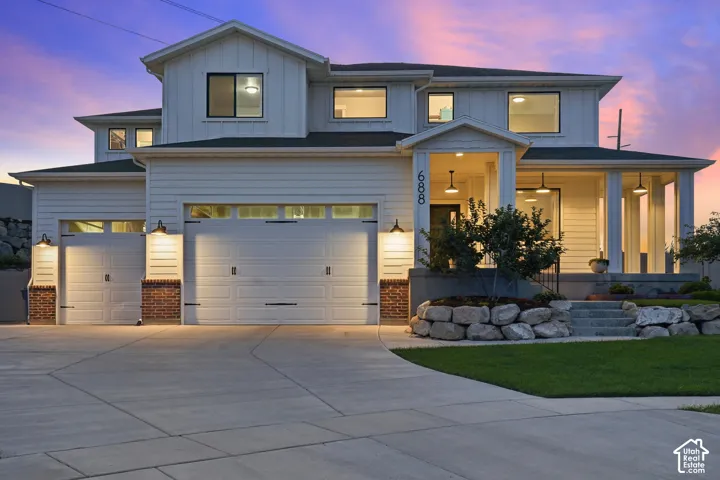 Modern farmhouse exterior featuring a covered porch, multiple garages, and a stone-edged landscape