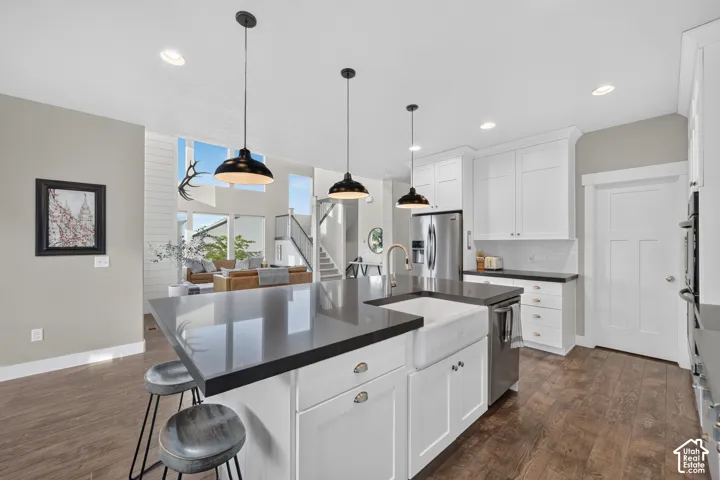 Open-concept kitchen with white shaker cabinetry, dark countertops, a large center island, and integrated stainless steel appliances