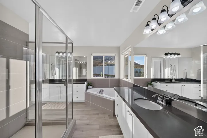Glass-enclosed shower, built-in soaking tub, dual vanity with undermount sinks, extensive countertop space, and large windows