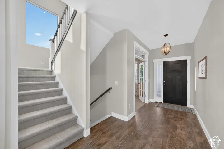 Wood-finish flooring leading to a carpeted staircase with a black handrail and white balusters