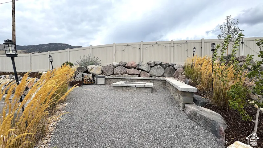 Gravel patio area featuring a built-in fire pit, stone retaining walls, and mature landscaping