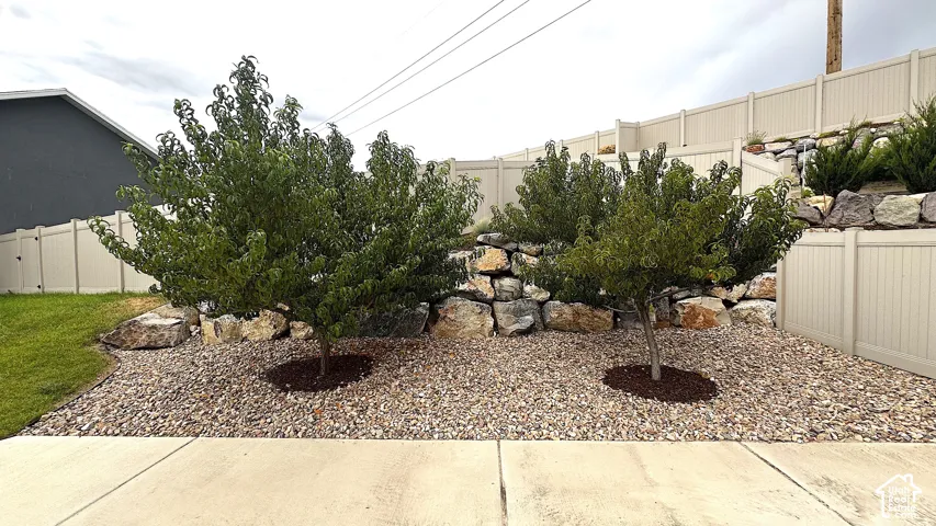 Decorative gravel landscaping with mature plantings, a concrete pathway, a rock retaining wall, and a privacy fence