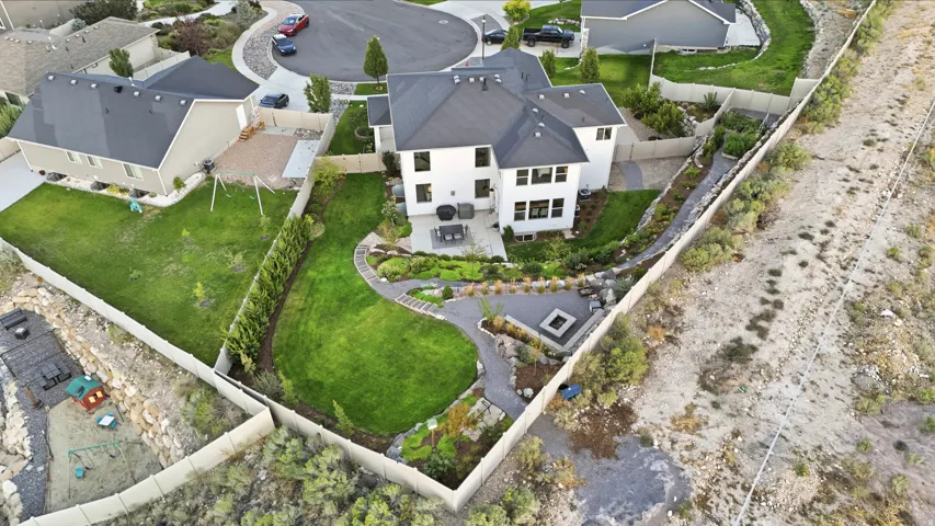 White exterior with dark roof, expansive green lawn, built-in fire pit, paved patio, and mature landscaping