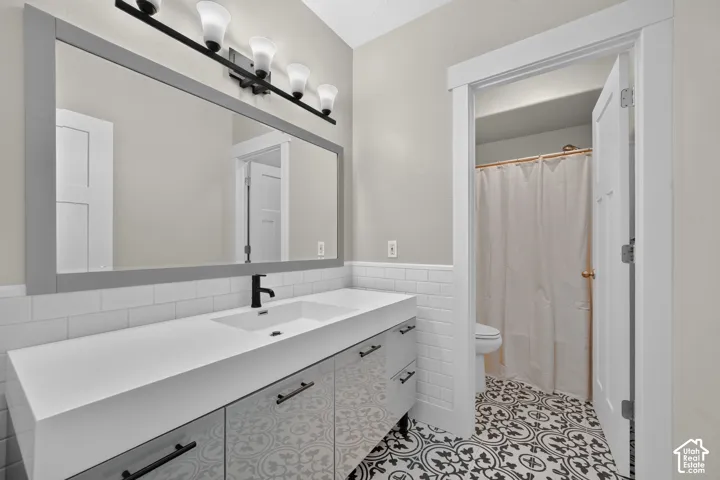 Bathroom featuring a single vanity with integrated sink, matte black faucet, wall-mounted light fixture, full-width framed mirror, and decorative patterned floor tiles