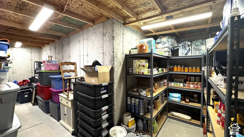 Unfinished basement area with concrete walls, exposed wood ceiling joists, and fluorescent lighting