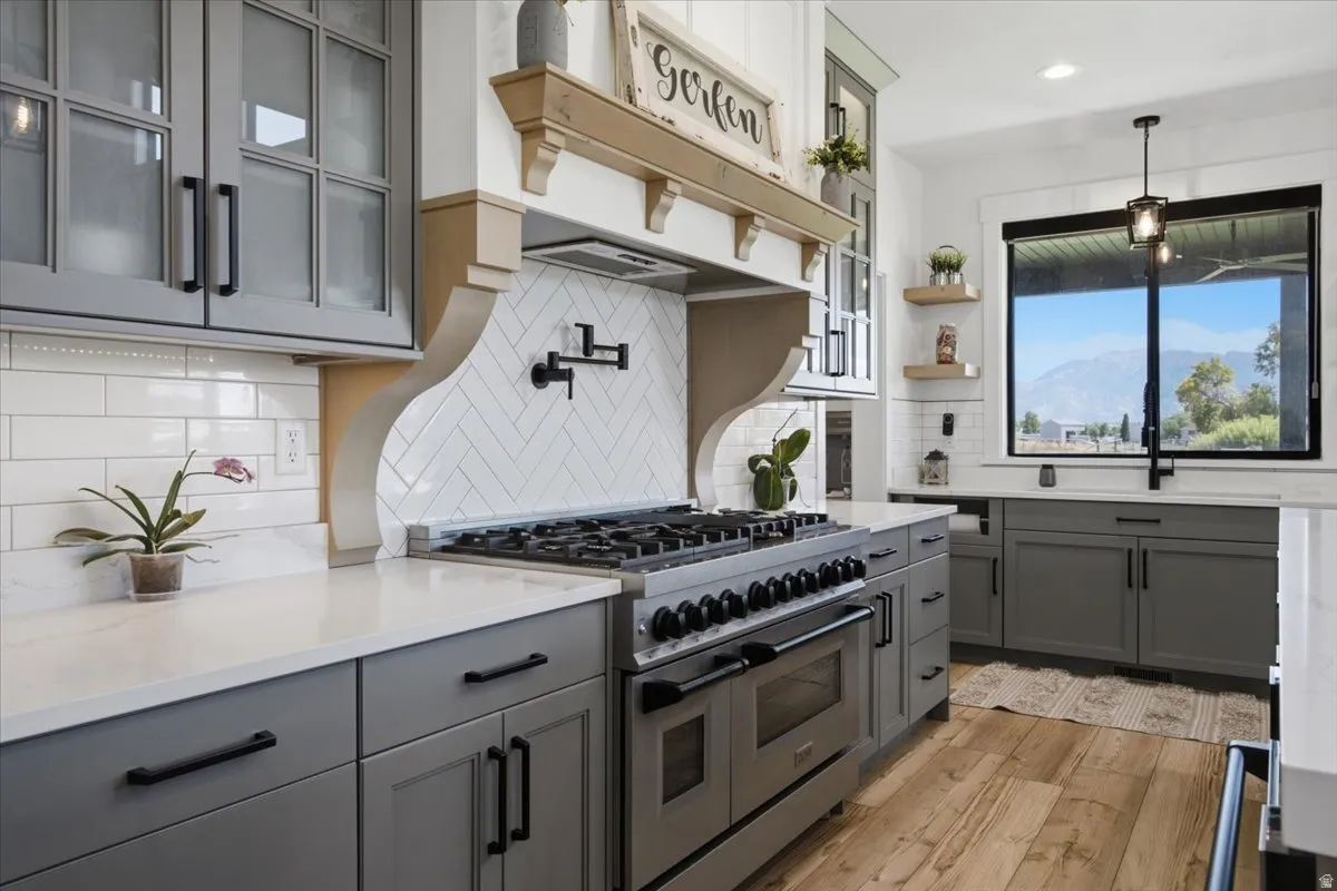 Gourmet kitchen featuring a professional-grade range, herringbone tile backsplash, and light wood-finish flooring