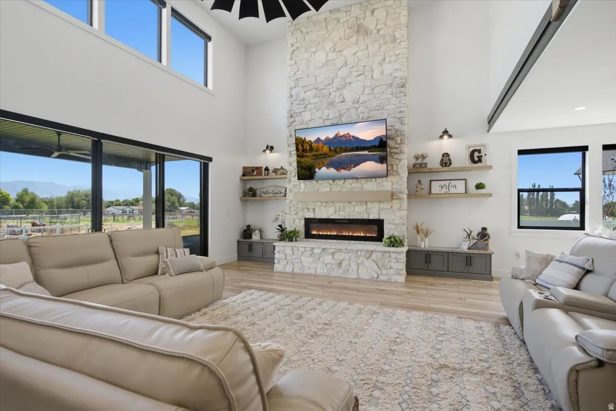 Vaulted ceiling with exposed beams, stone-clad fireplace with electric insert, large format sliding glass doors, upper transom windows, and wood-finish flooring