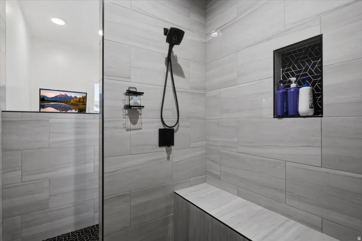 Shower featuring large format tile, built-in bench, recessed shower niche with patterned tile, and a matte black shower fixture