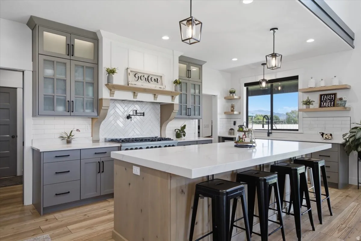 Spacious kitchen featuring an expansive central island, a herringbone tile backsplash, gray and white cabinetry, wood-finish flooring, and recessed lighting