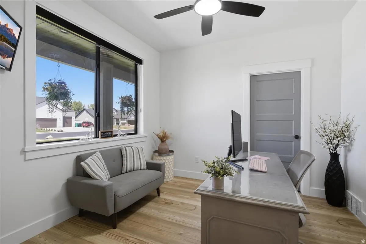 Bright room featuring wood-finish flooring, a contemporary ceiling fan, and a wide window with a black frame