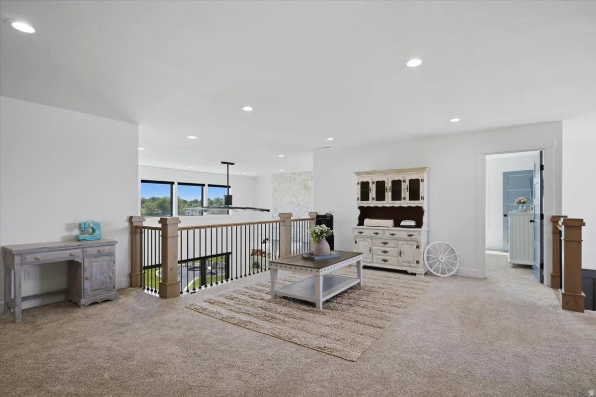 Carpeted loft area with recessed lighting, black metal and wood railing, and multiple windows