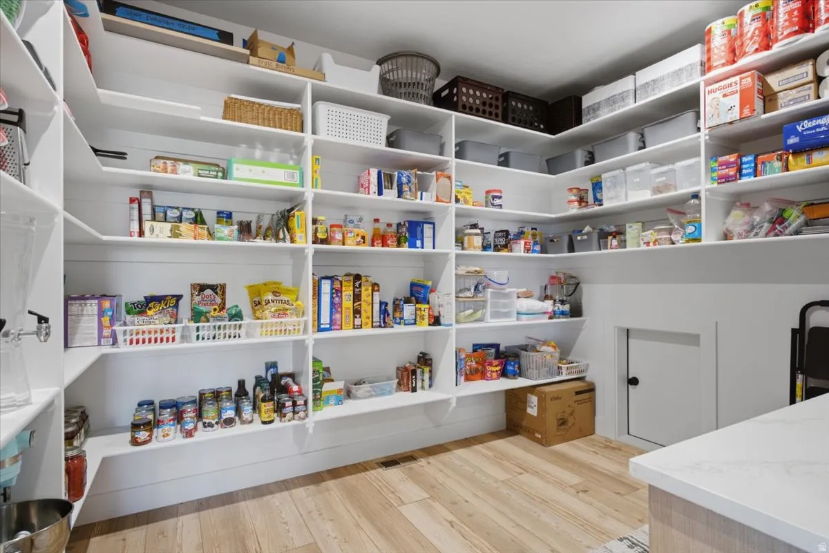Expansive walk-in pantry featuring abundant built-in shelving, durable wood-finish flooring, and bright white walls