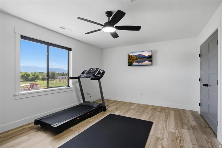 Wood-finish flooring, a ceiling fan with integrated lighting, and a window with a roller shade