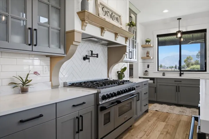 Gourmet kitchen featuring a professional-grade range, herringbone tile backsplash, and light wood-finish flooring