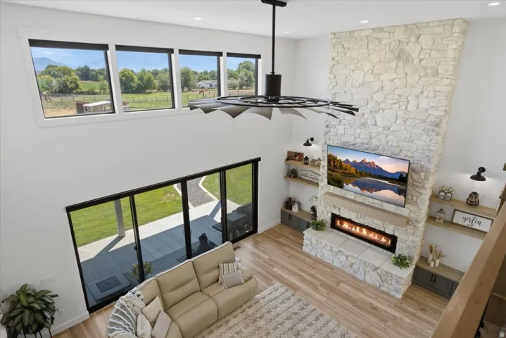 Two-story living area featuring a stone accent wall with a built-in fireplace, a ceiling fan, and wood-finish flooring