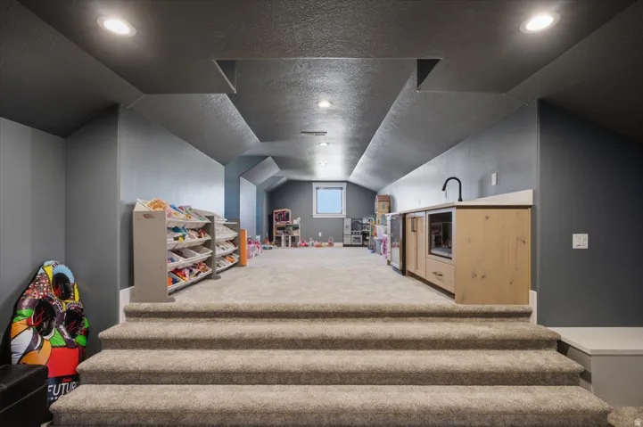Carpeted staircase leading to a spacious room with a built-in wet bar, recessed lighting, and a window