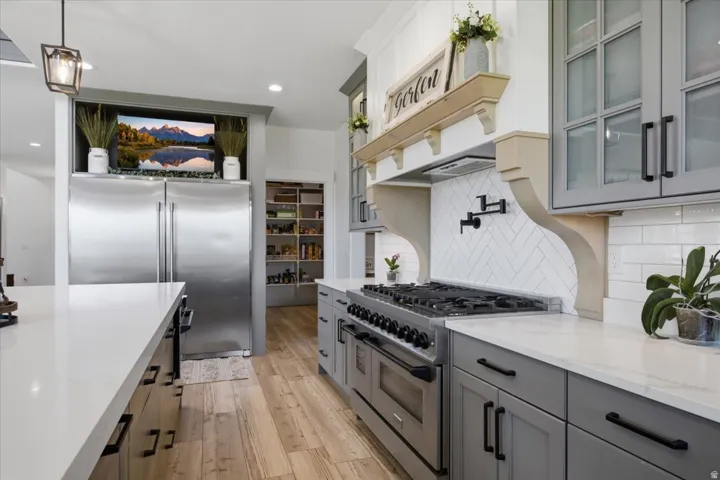 Gourmet kitchen featuring stainless steel appliances, herringbone tile backsplash, gray cabinetry, light-colored countertops, and wood-finish flooring