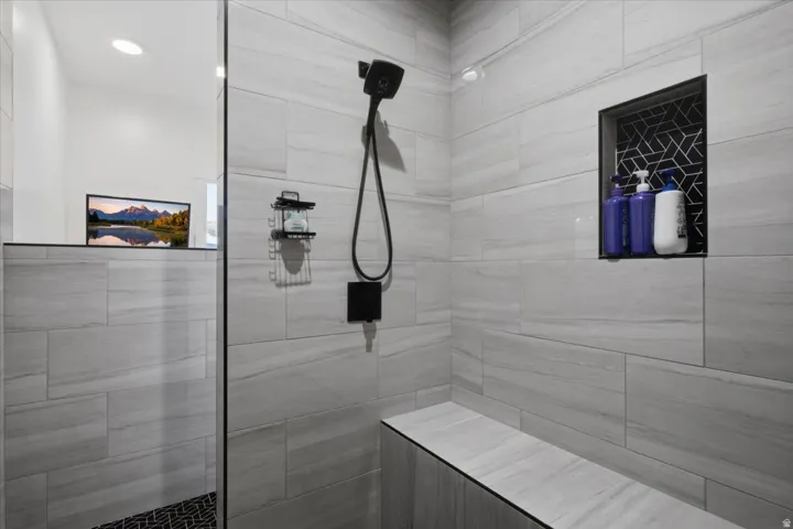 Shower featuring large format tile, built-in bench, recessed shower niche with patterned tile, and a matte black shower fixture