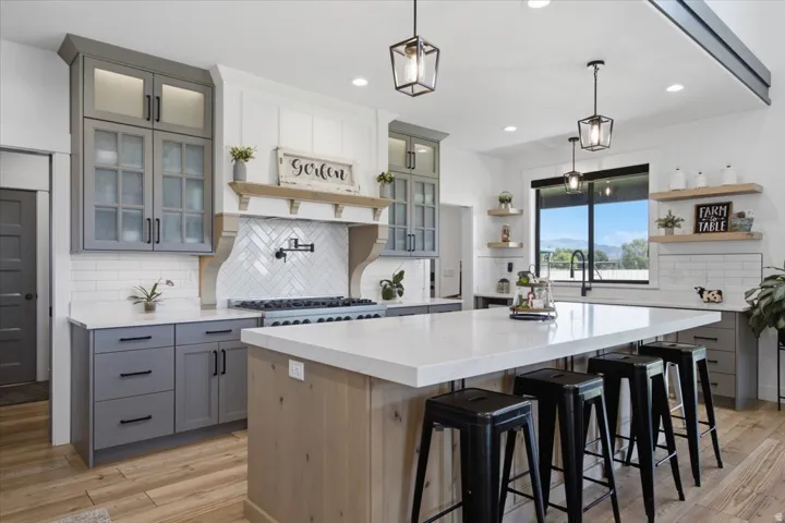 Spacious kitchen featuring an expansive central island, a herringbone tile backsplash, gray and white cabinetry, wood-finish flooring, and recessed lighting