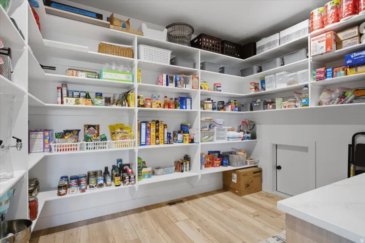 Expansive walk-in pantry featuring abundant built-in shelving, durable wood-finish flooring, and bright white walls