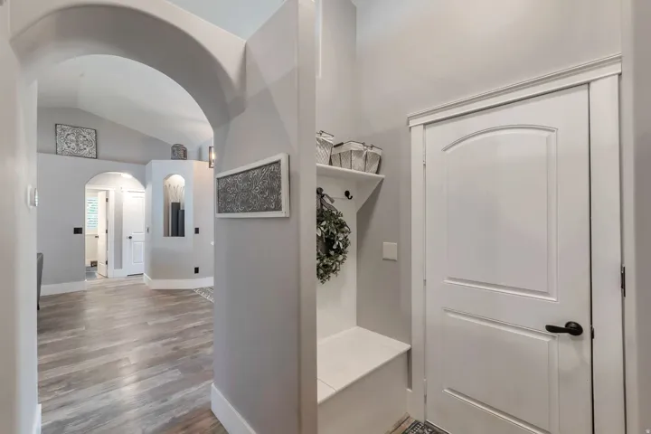 Archway entry leading to wood-finish flooring, featuring a built-in bench and shelving