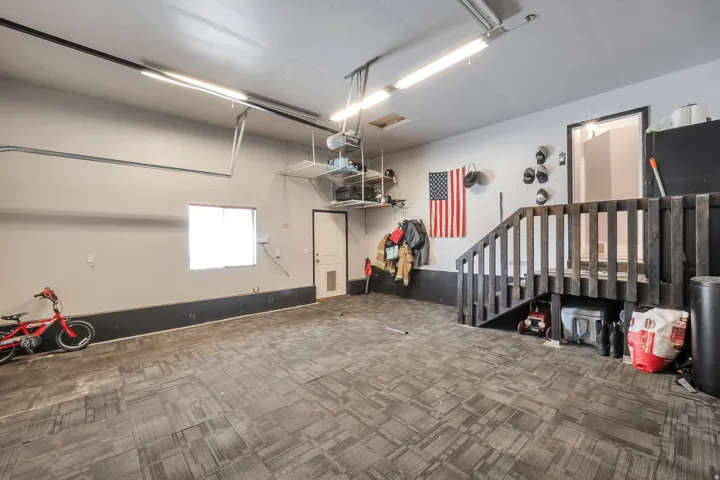 Spacious garage featuring carpet-tile flooring, overhead fluorescent lighting, and a built-in wooden staircase