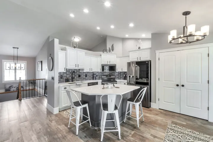 Recessed ceiling lights, wood-finish flooring, white cabinetry, dark subway tile backsplash, and a central island with a white countertop