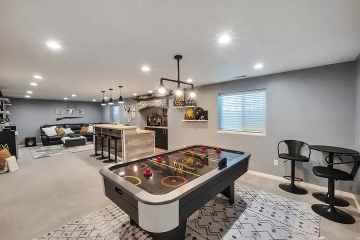 Recessed lighting, wood-finish bar with pendant lights, built-in shelving, carpeted flooring, and a window with blinds