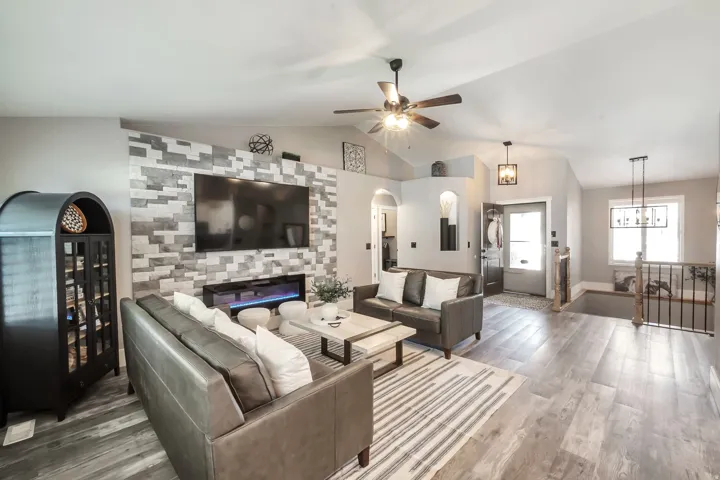 Vaulted ceilings, wood-finish flooring, stone accent wall with electric fireplace, ceiling fan, and modern pendant lighting