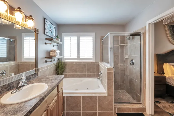 Built-in soaking tub with tile surround, glass-enclosed shower with tiled walls, single vanity with integrated sink and countertop, and integrated wall shelving
