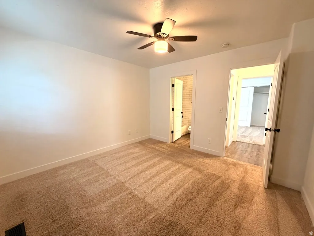 Plush carpeting throughout, neutral wall finishes, and a ceiling fan with integrated lighting