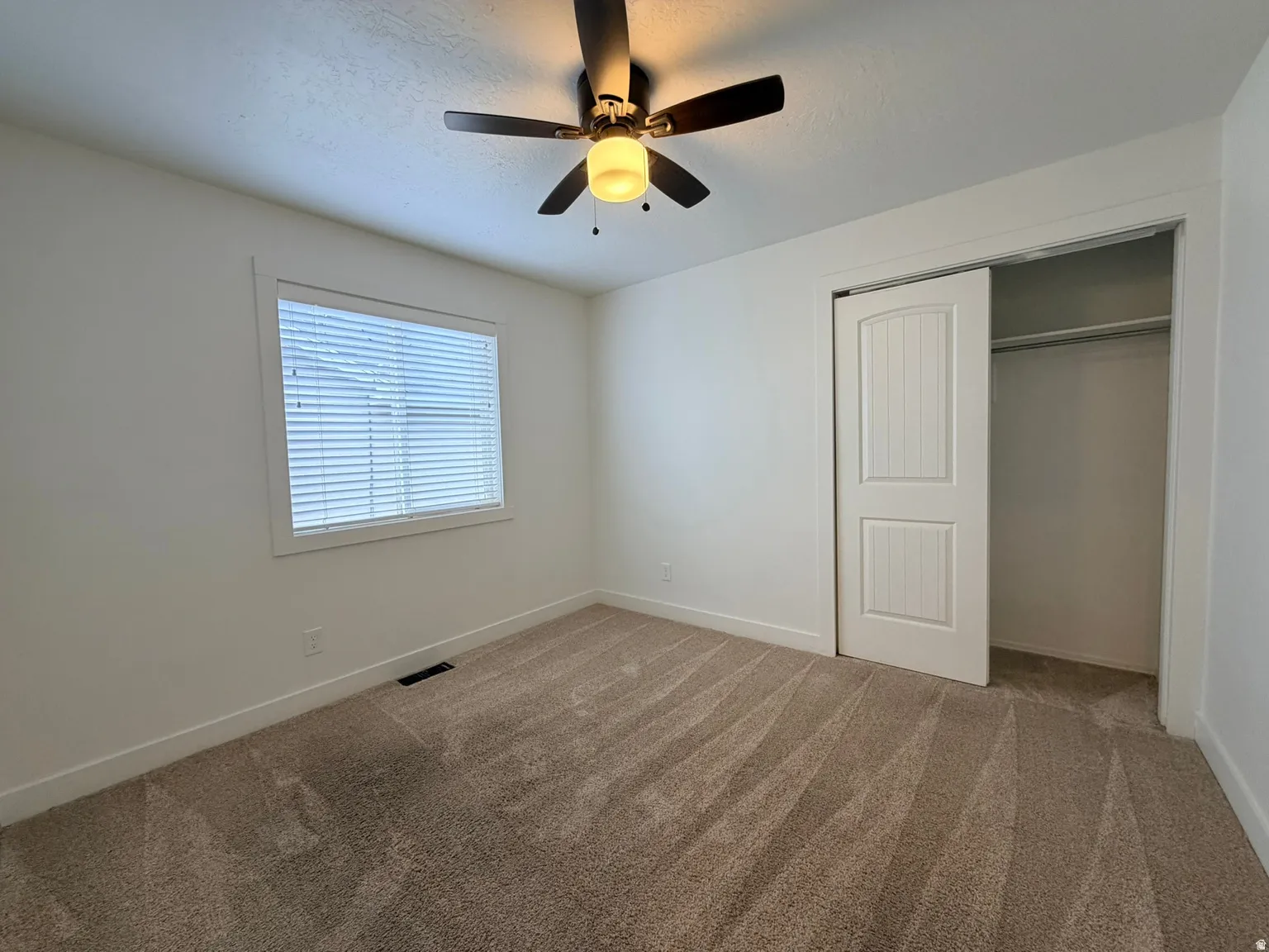 Bright secondary bedroom featuring neutral carpeting, a ceiling fan with integrated lighting, and a spacious walk-in closet with bifold doors and shelving
